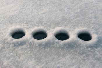 Straight line of drilled ice holes stretching across a flat surface