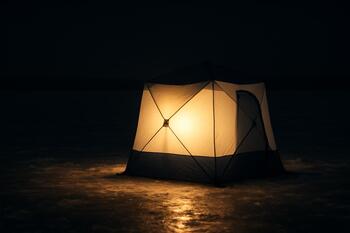 Lantern glowing on the ice beside an angler at night