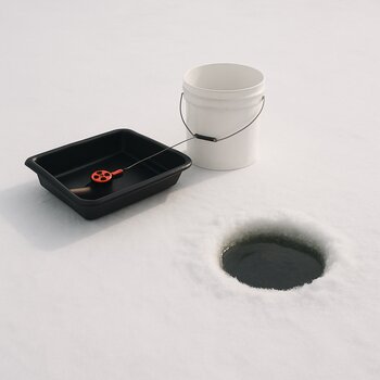 Minimalist ice kit with a small sled beside a drilled hole